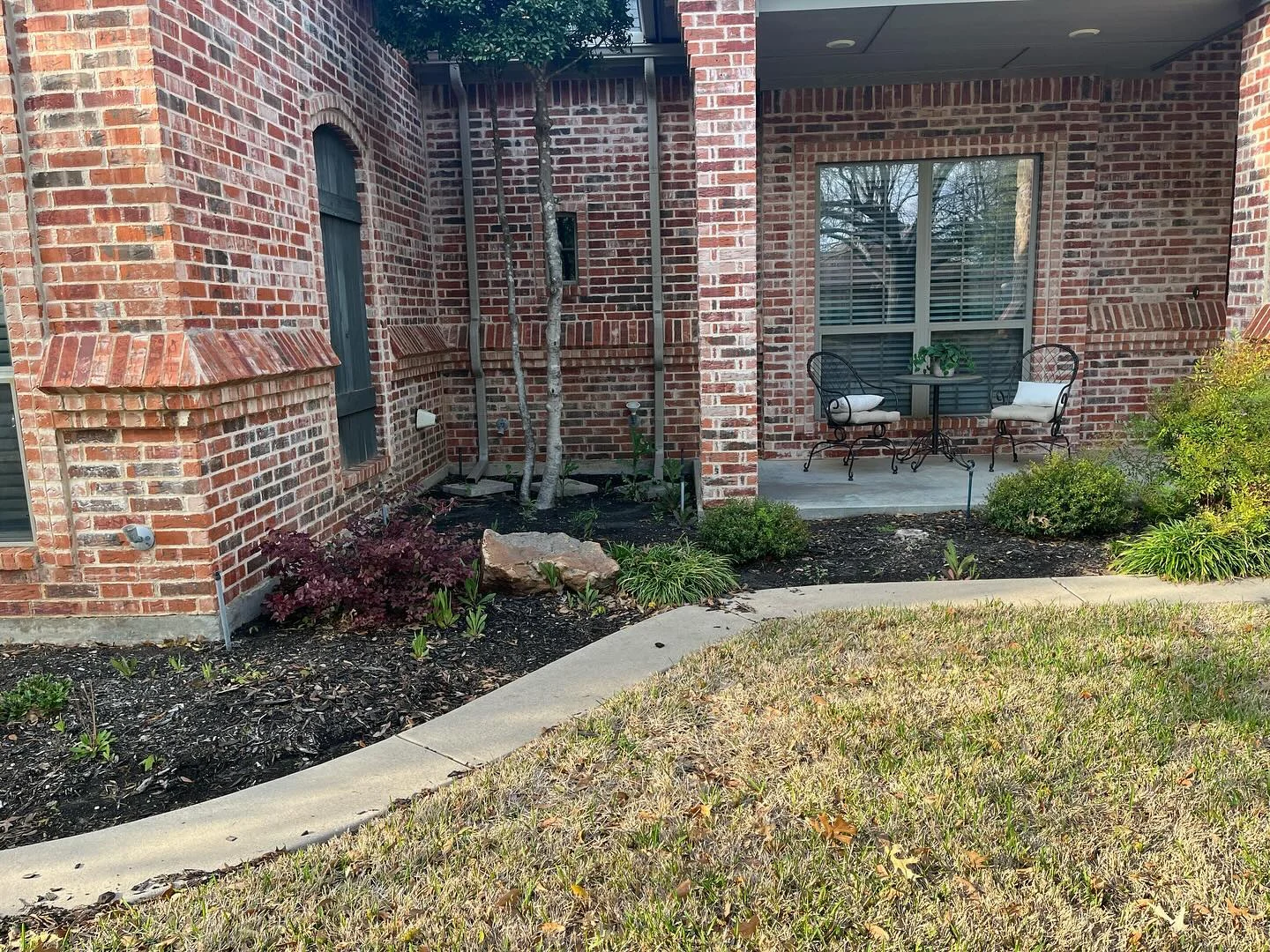 Planted flowerbeds around a curving path beside a red brick home