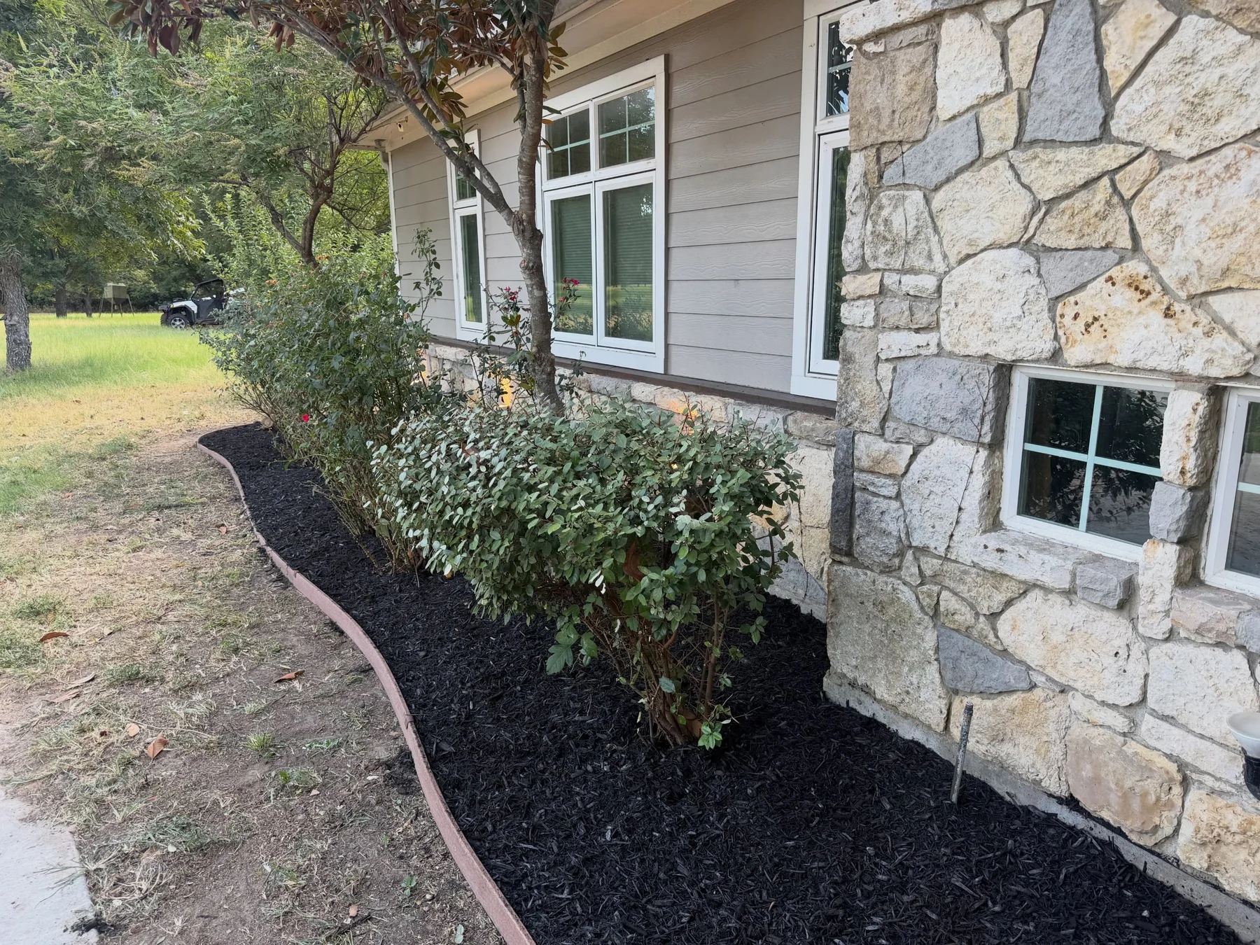 Cleaned flowerbed with black mulch beside a Decatur stone and siding home